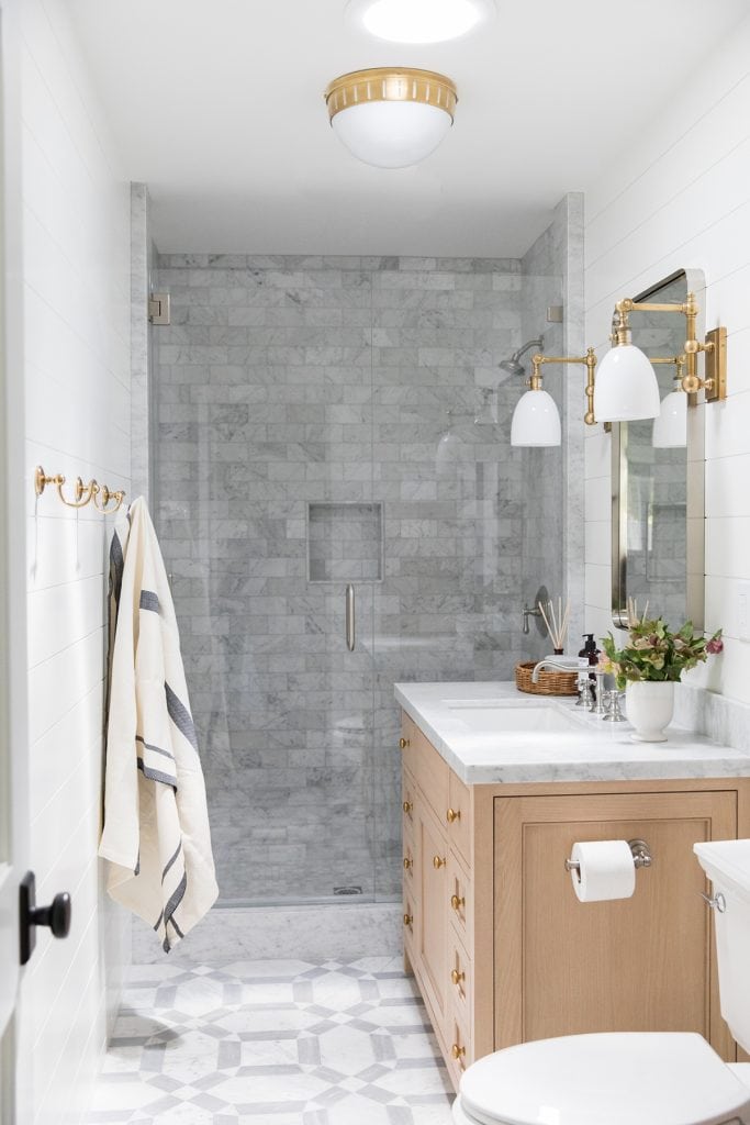 bathroom with patterned marble floor tile and marble subway wall tile with light wood vanity and mixed metals