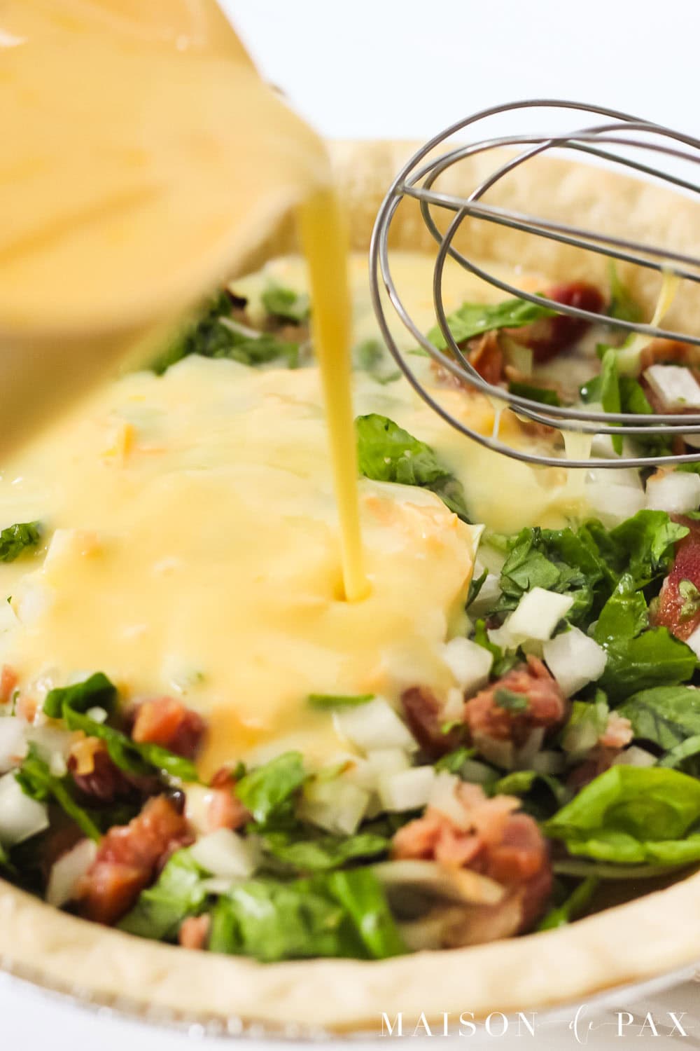 pouring egg mixture over ham and spinach in a pie crust