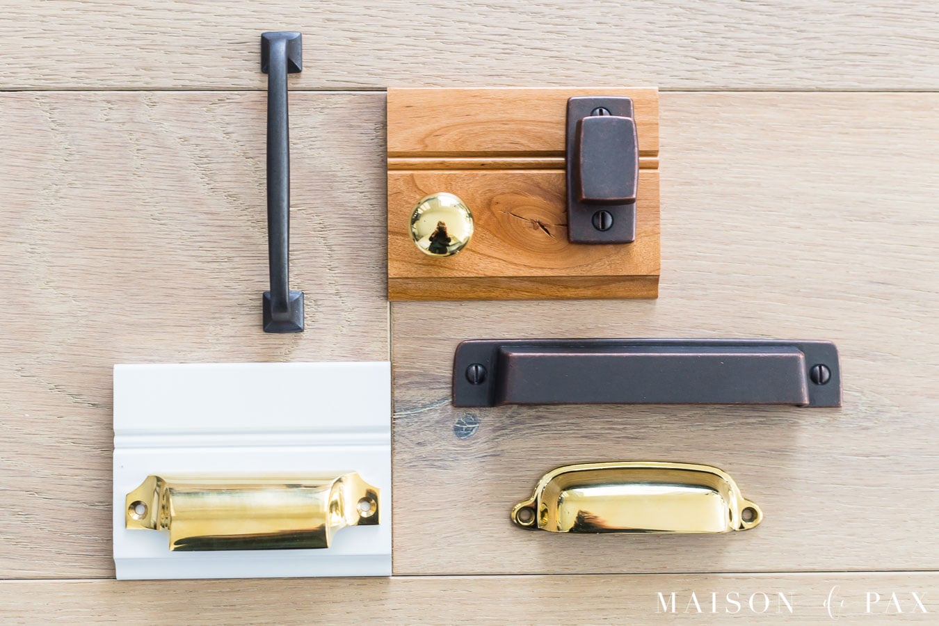 oil rubbed bronze and brass hardware samples laid out with rustic alder and white cabinet samples on wide plank oak flooring