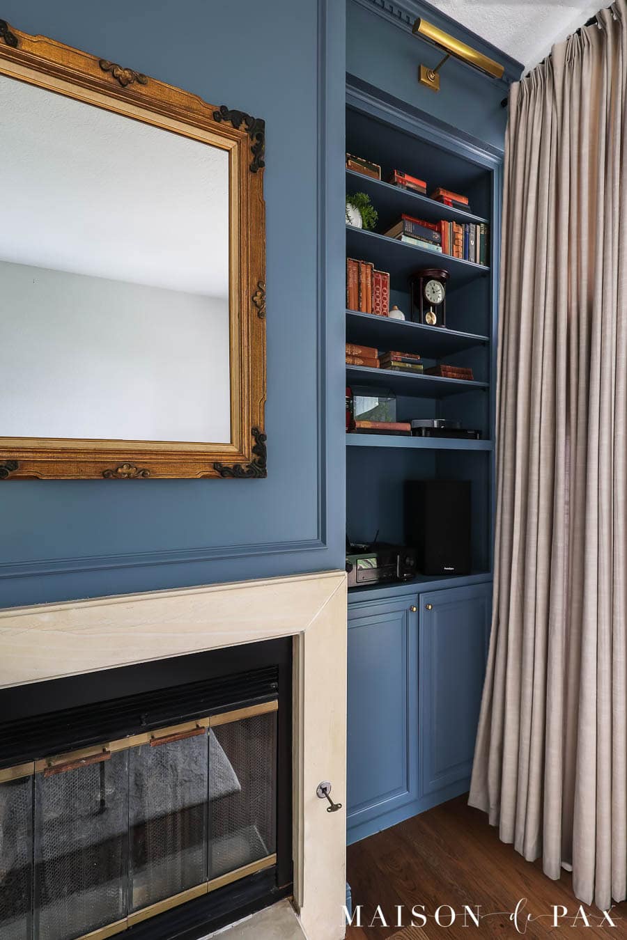 moody blue bookcases on either side of limestone fireplace with antique mirror hung above