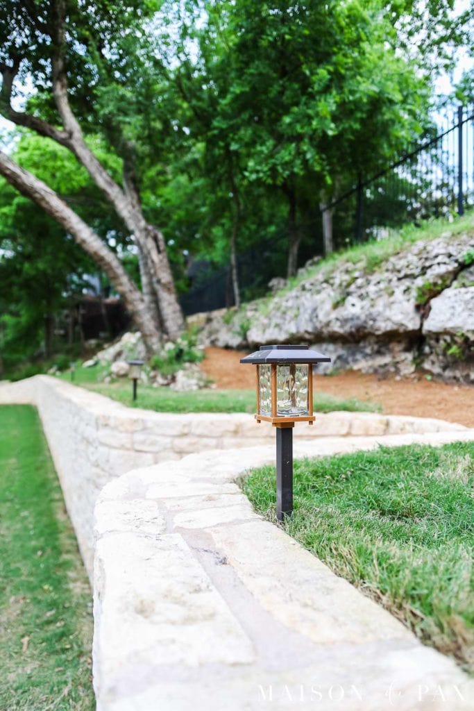 solar lantern pathway light in backyard beside limestone retaining wall