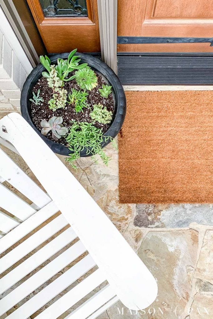 wood front door, brown door mat, black planter with succulents, and white adirondack chair | Maison de Pax