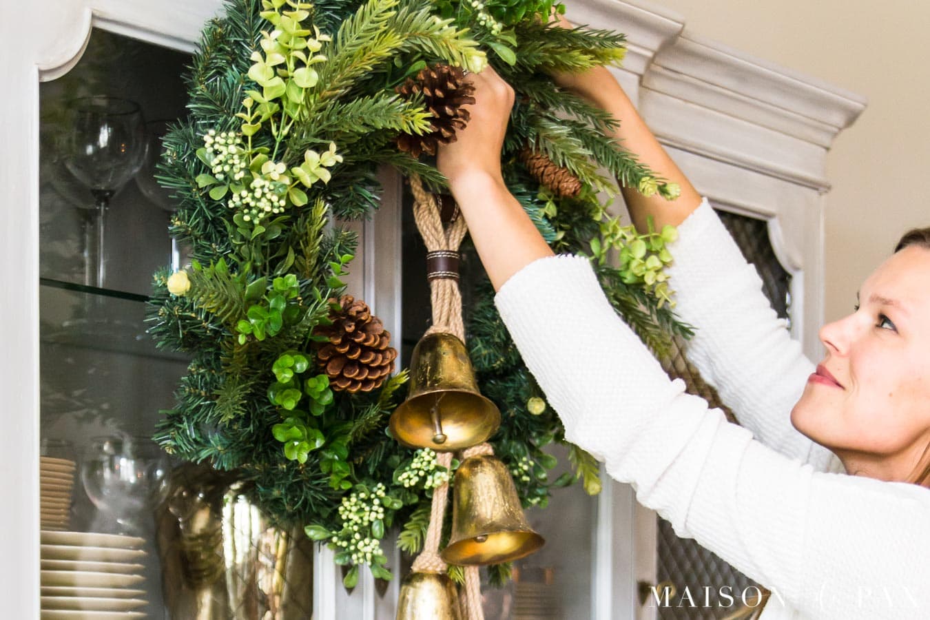 woman hanging greenery wreath with gold jingle bells | Maison de Pax