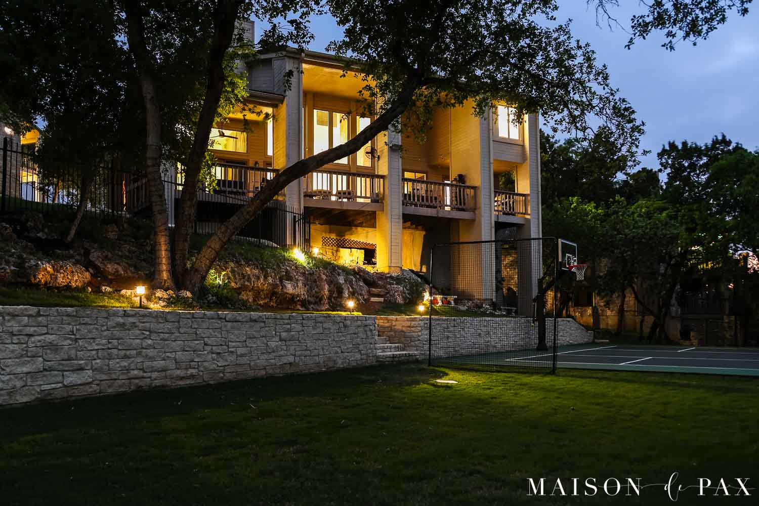 backyard lit up at night with sport court and large porch