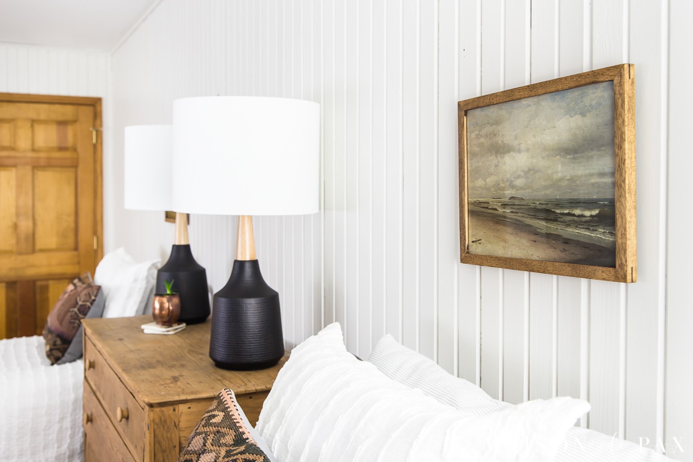 vintage beach landscape art above antique bed against white planked walls | maison de pax