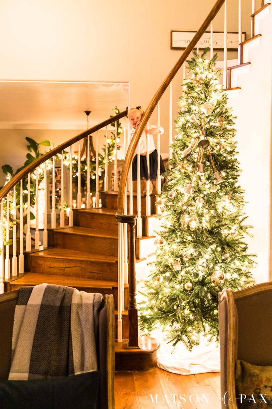 little girl on stairs beside huge lit Christmas tree | Maison de Pax