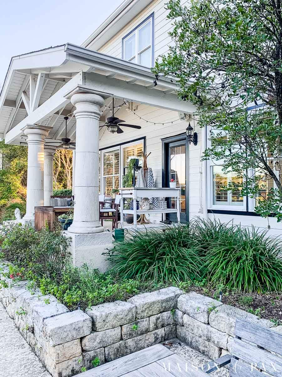 stone garden border in back of white house with large porch and black trim | Maison de Pax