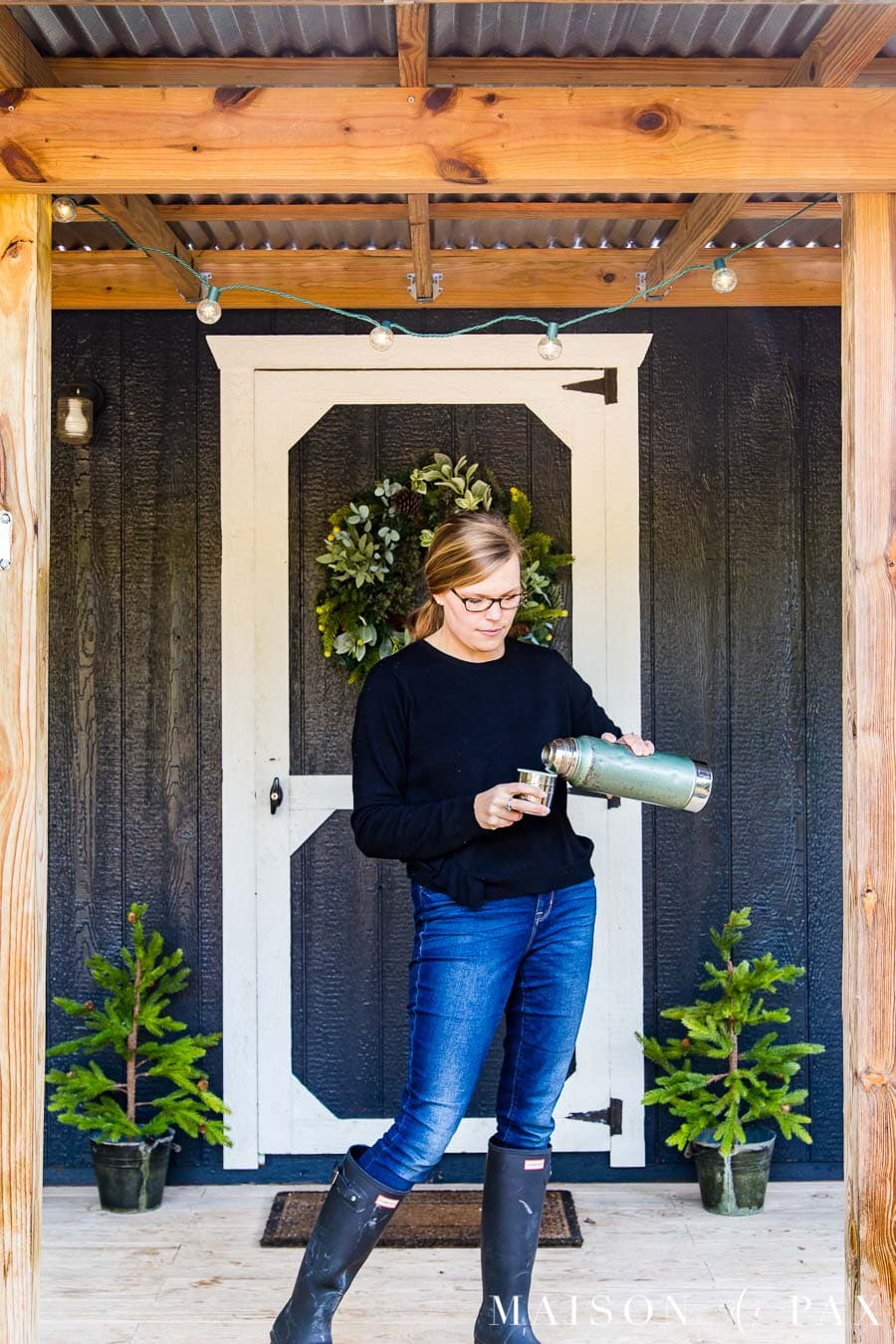 woman pouring coffee from an old thermos on the front porch of a black and white farmhouse