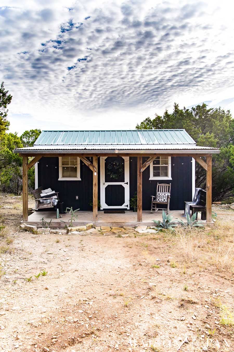 tiny black house with white trim and cedar posts over a porch