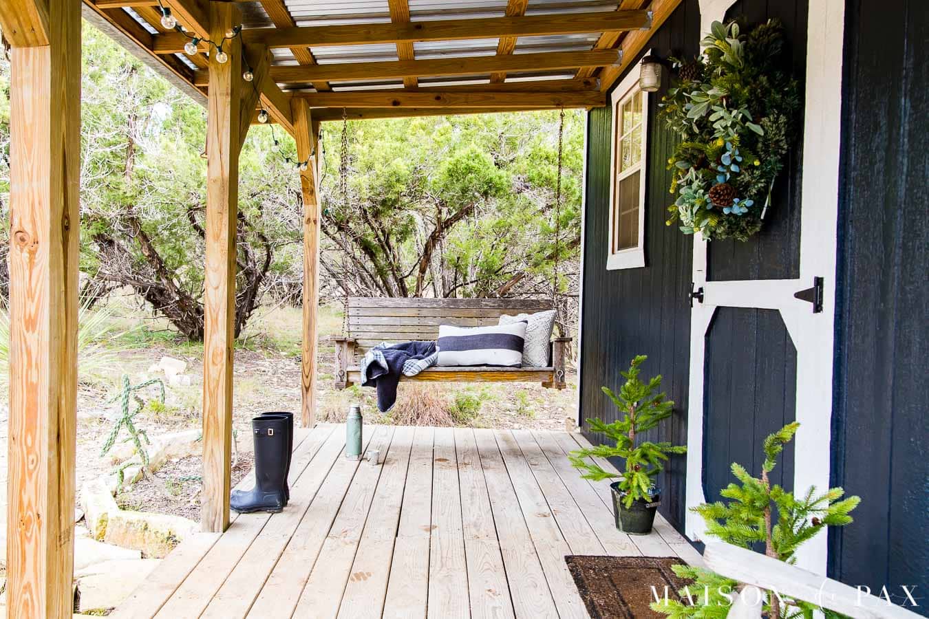 old wood porch swing with black and white outdoor pillows on a farmhouse porch decorated for Christmas