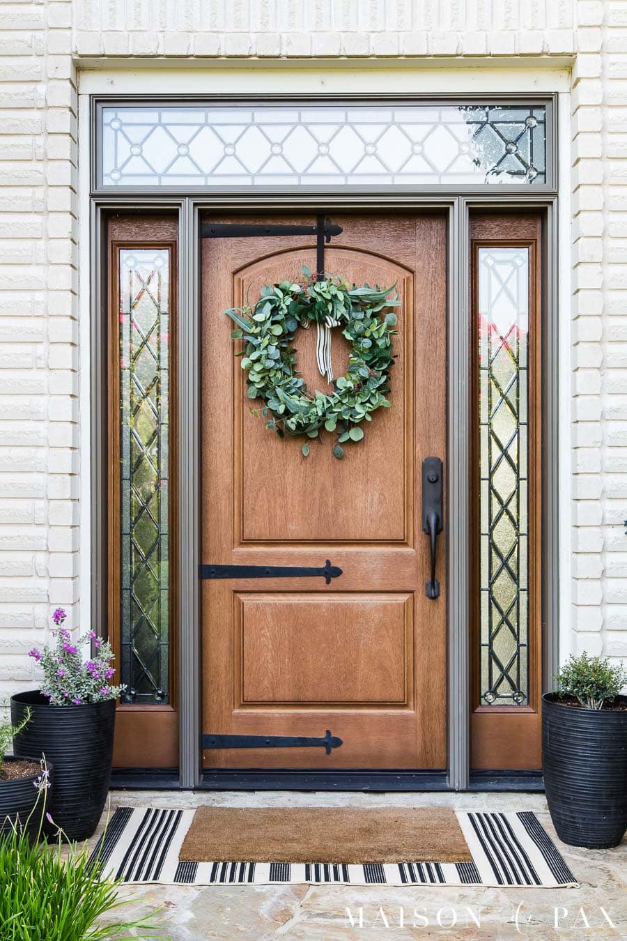 cream brick house with wood door and black pots | Maison de Pax