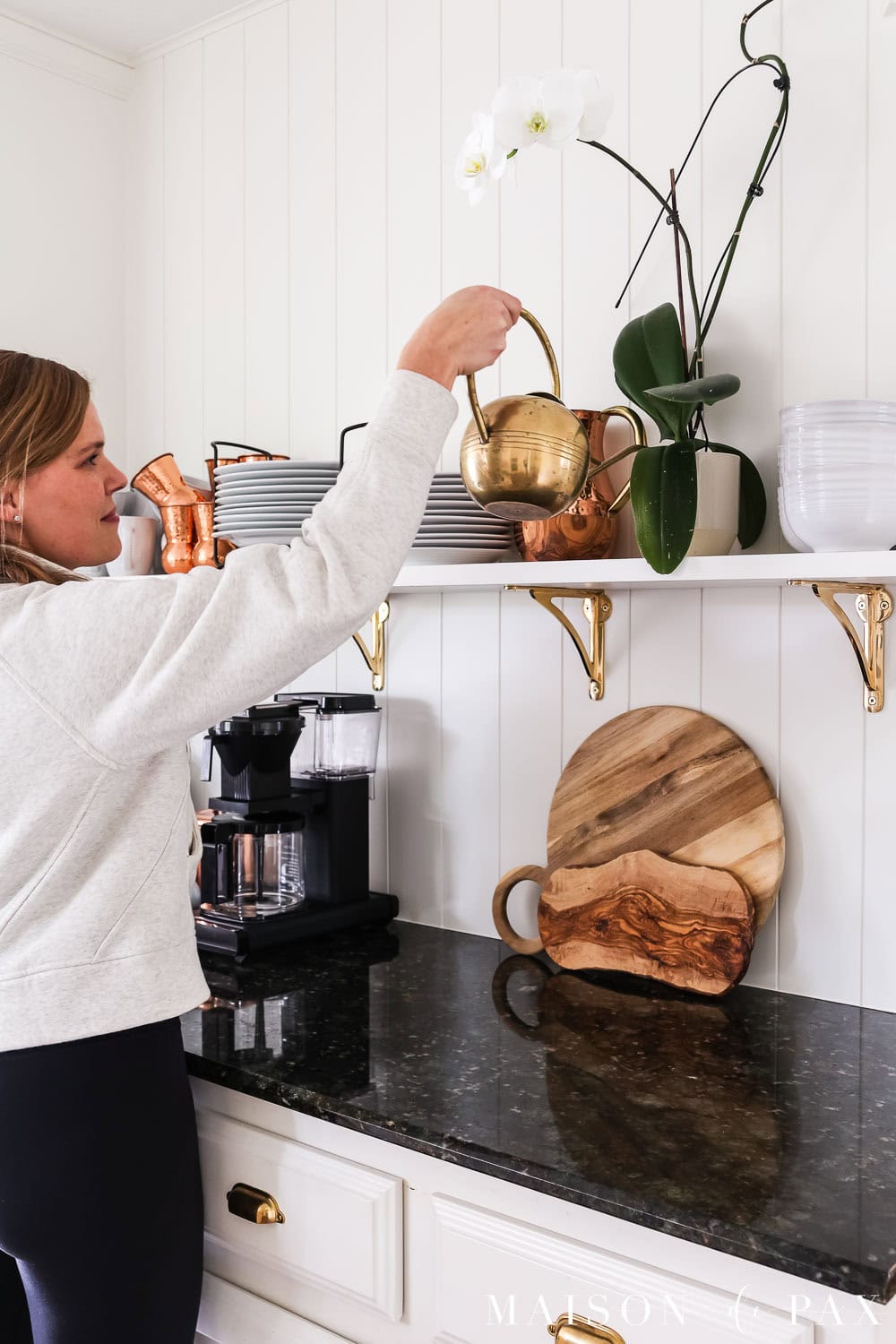 watering a houseplant on a shelf with dishes in the kitchen