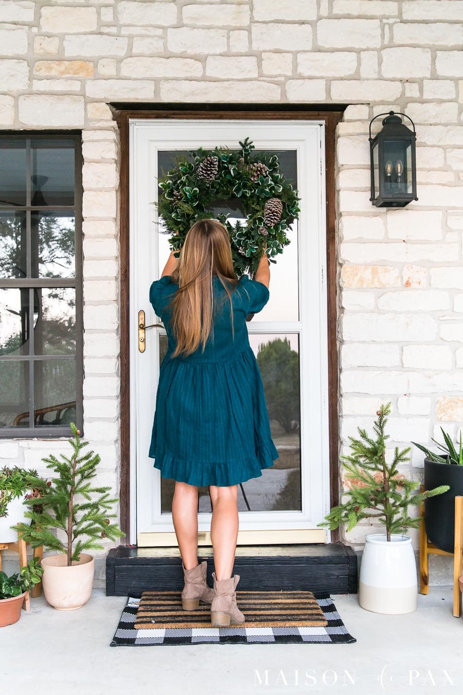 woman hanging wreath on storm door on farmhouse porch | Maison de Pax