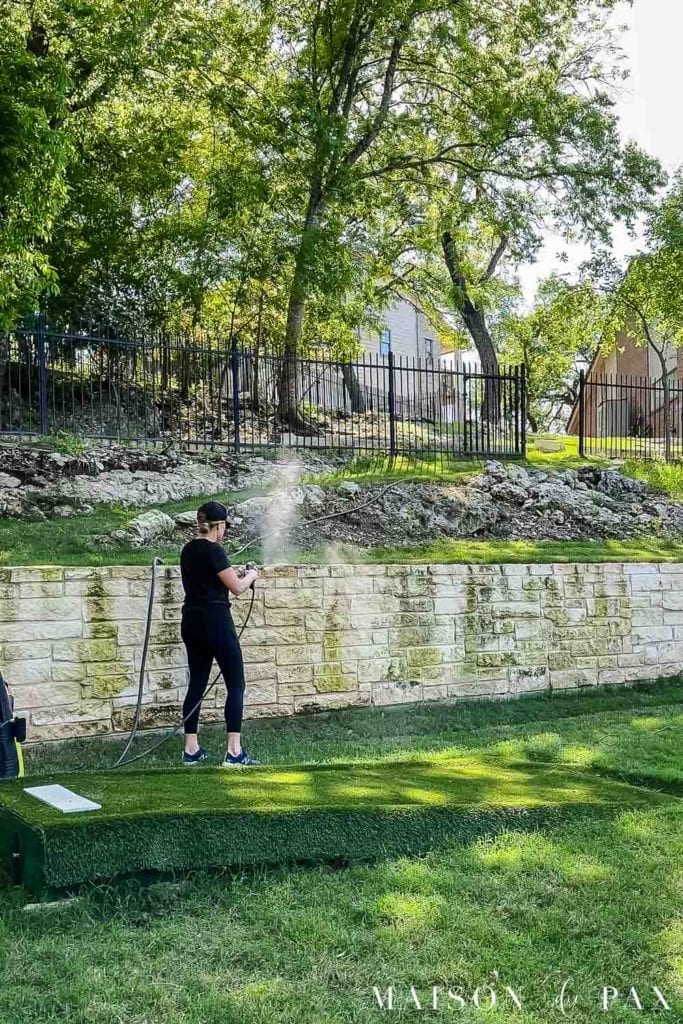 woman pressure washing limestone wall to remove mildew and discoloration 