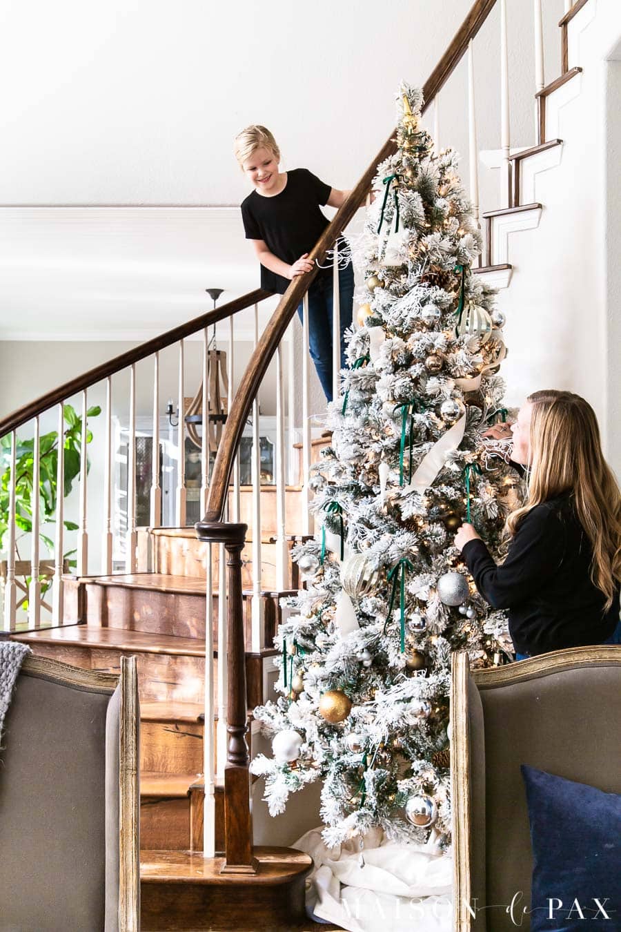 mother and daughter decorating large flocked Christmas tree in stairwell | Maison de Pax