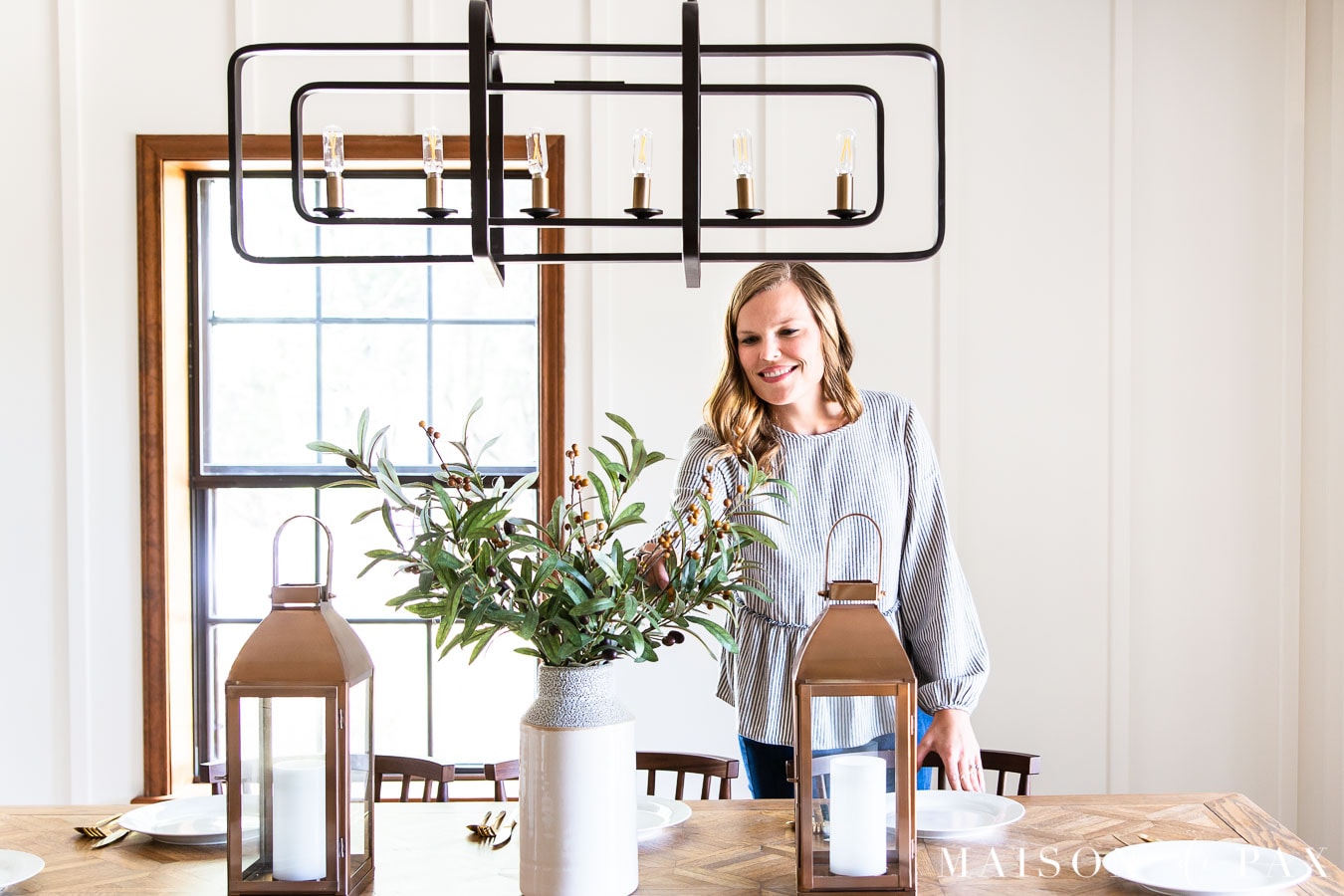 woman putting olive branches in white vase on wood dining table | Maison de Pax