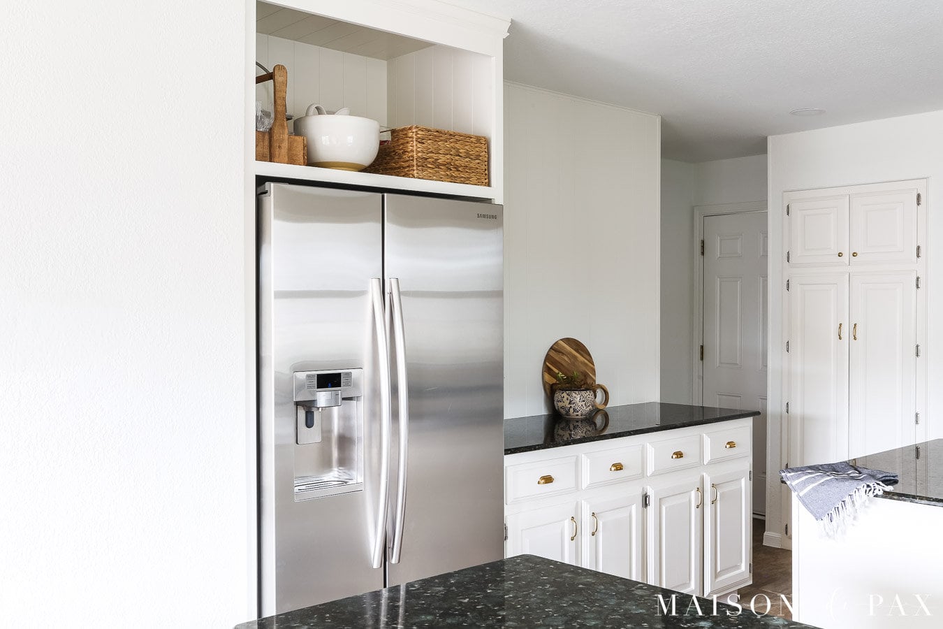 white kitchen with vertical nickel gap walls and open cabinet above fridge
