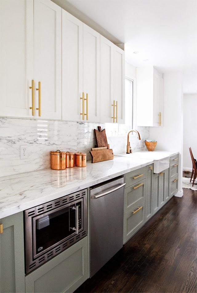 kitchen with gray lower cabinets and white uppers with brass hardware and marble countertops