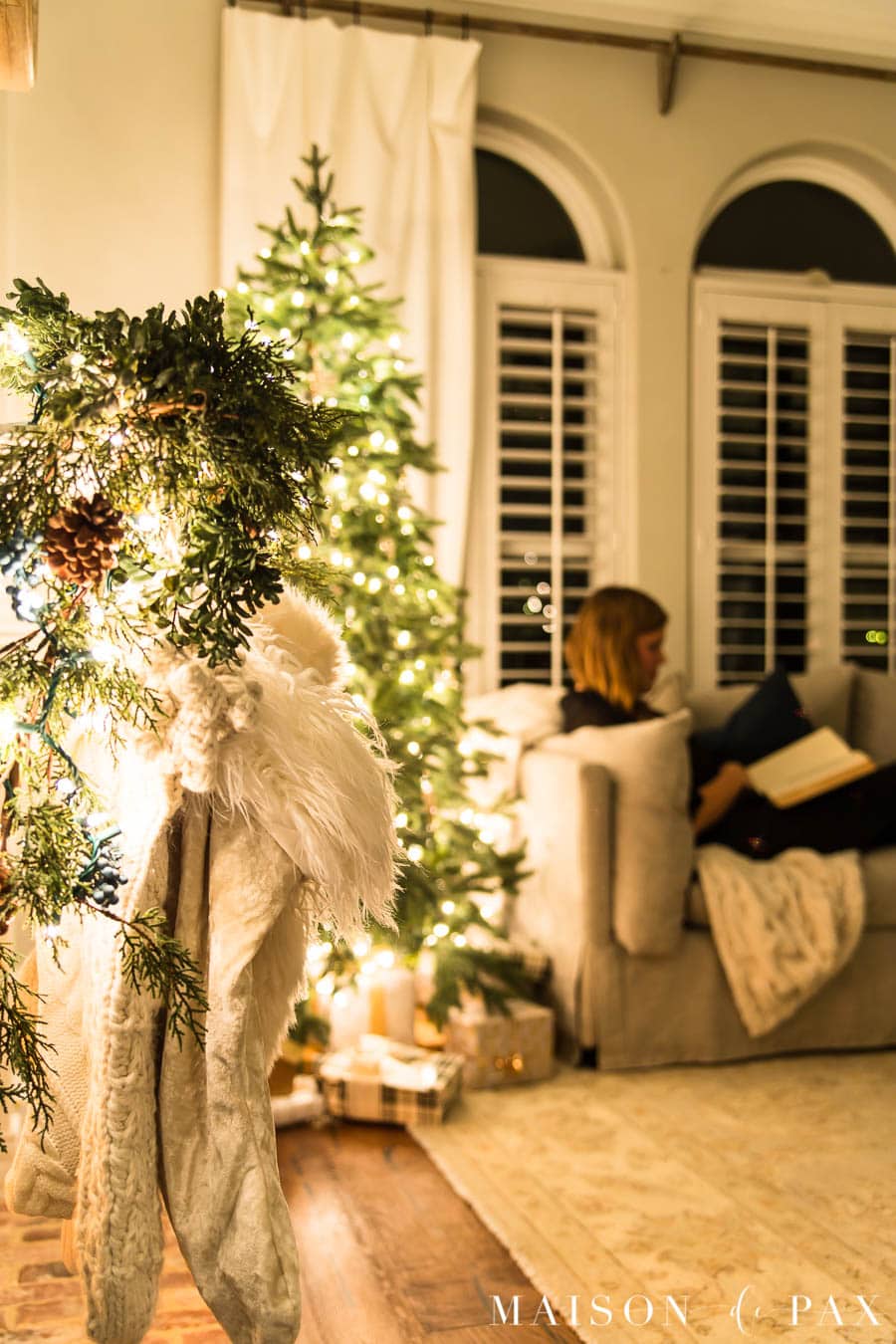 woman reading on couch beside Christmas tree at night | Maison de Pax