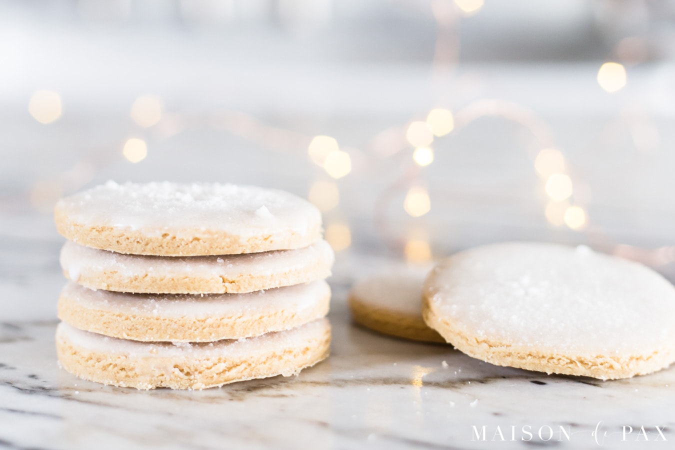 stacked iced cookies with sugar sprinkled on top and christmas lights | maison de pax