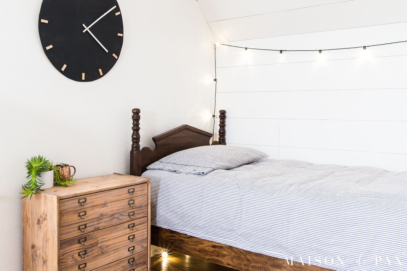 white bedroom with planked wall, antique twin bed, and printer's cabinet nightstand