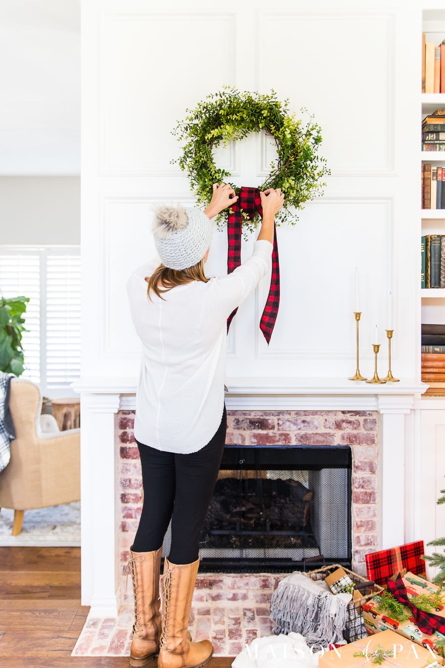 woman hanging wreath above mantel with red buffalo plaid ribbon | Maison de Pax