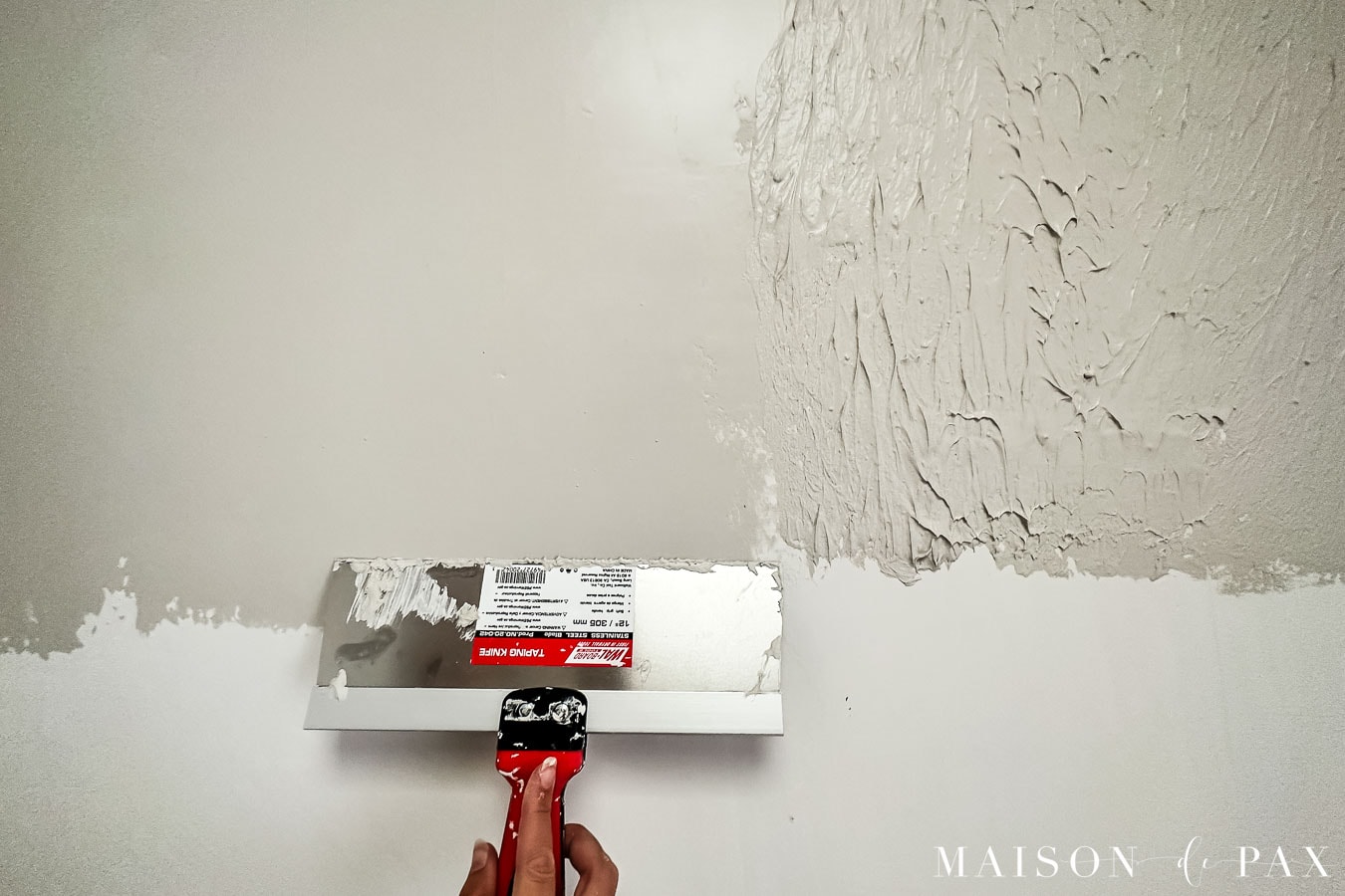 using a large taping knife to smooth joint compound for smooth wall texture