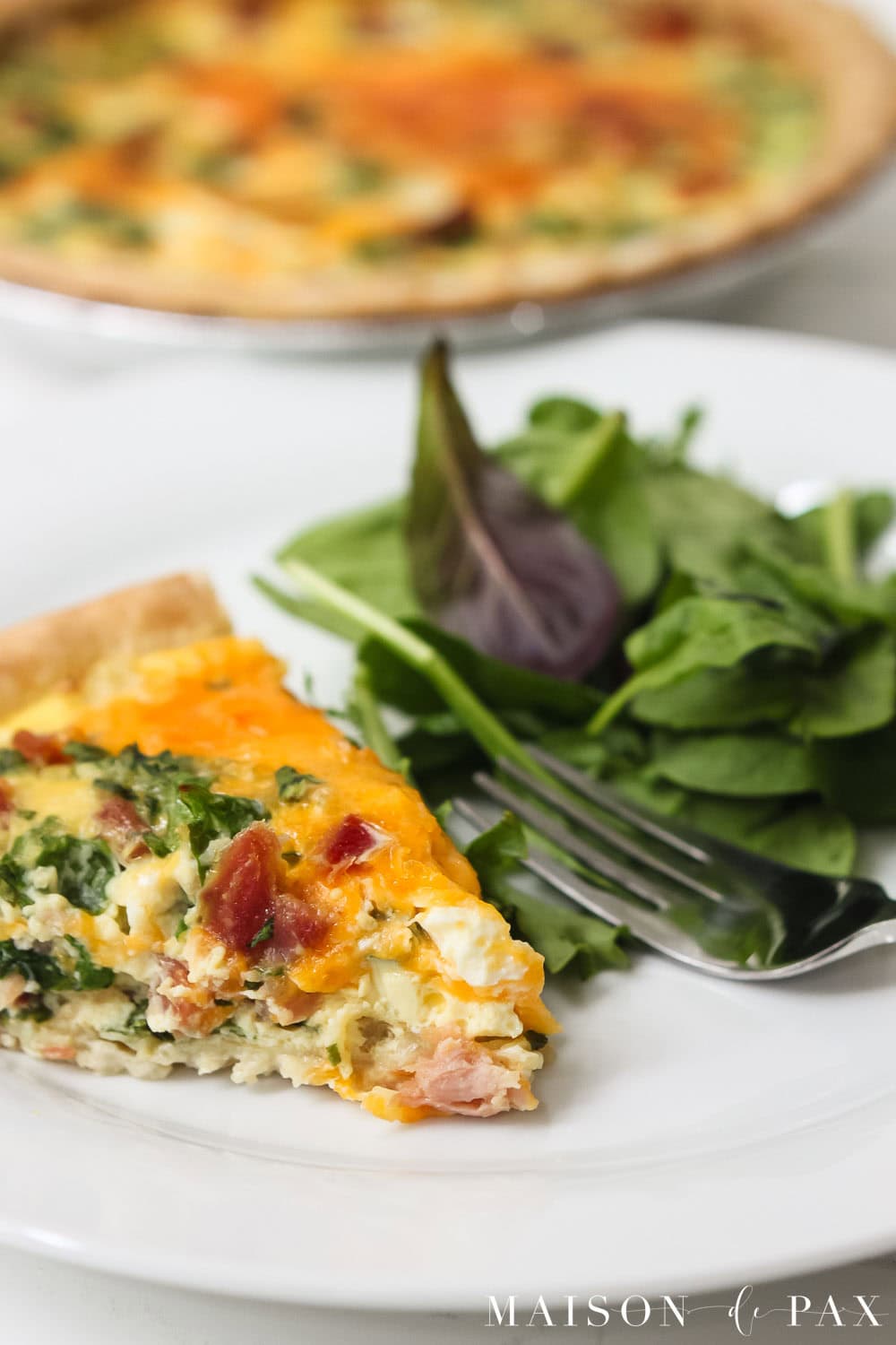 slice of cheesy ham and spinach quiche with a side salad
