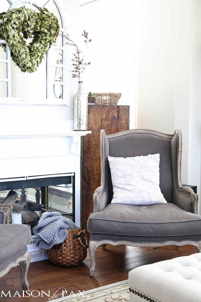 beautiful, neutral living room with gray wingback chairs, natural textures, white fireplace, and a gorgeous wreath 