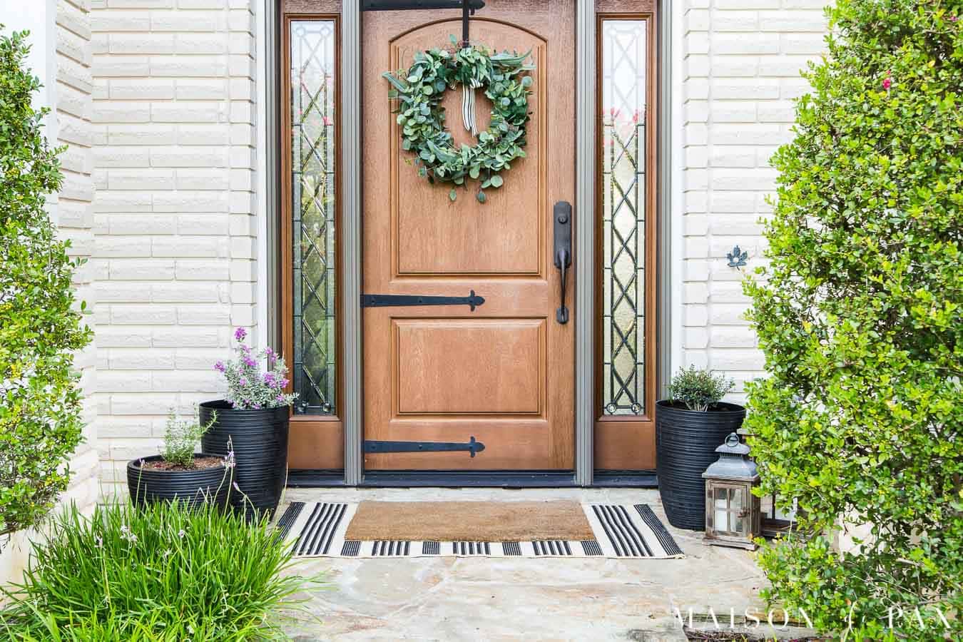 black pots on front porch with wood door and white brick | Maison de Pax