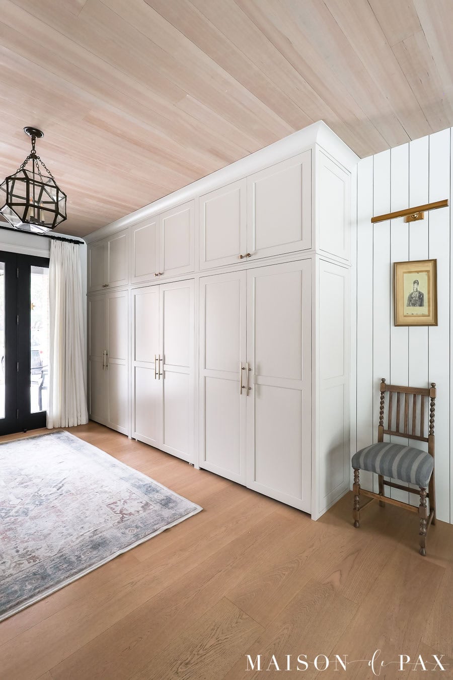 entryway with greige cabinetry, antique chair, vintage art, and a library sconce