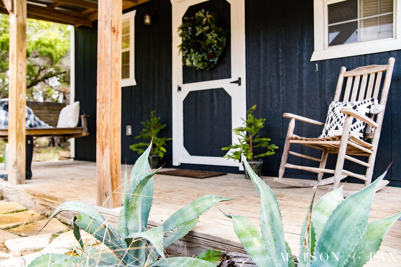 agave plants in the foreground and a black and white tiny farmhouse porch in the background