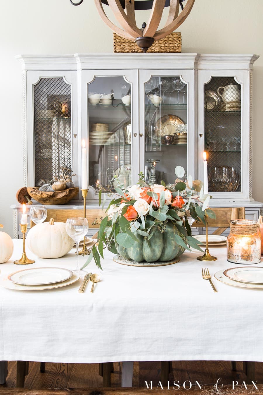 french country china hutch behind an elegant Thanksgiving table with white tablecloth, pumpkin centerpiece, and gold and silver china