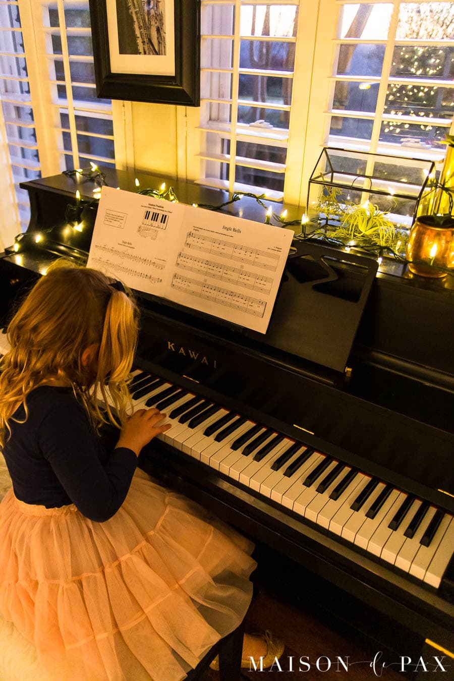 girl playing jingle bells on piano with Christmas lights | Maison de Pax