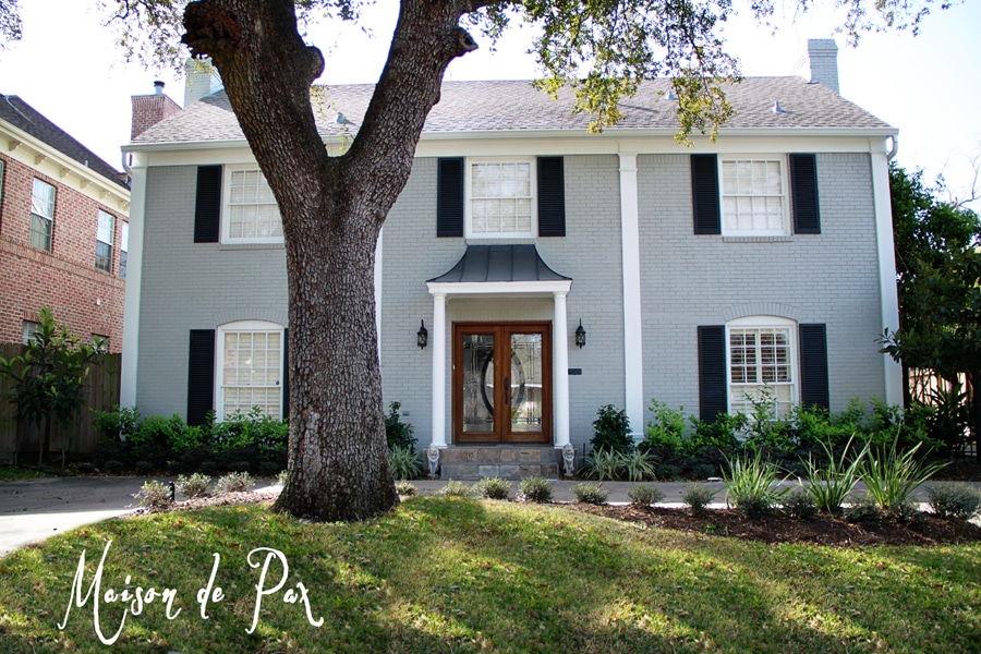 Gray and white painted brick colonial home with black shutters- Maison de Pax