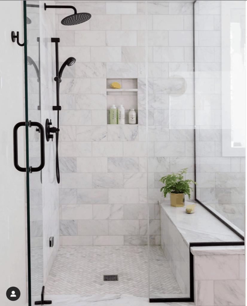 carrara marble shower with black plumbing fixtures and shower door frame