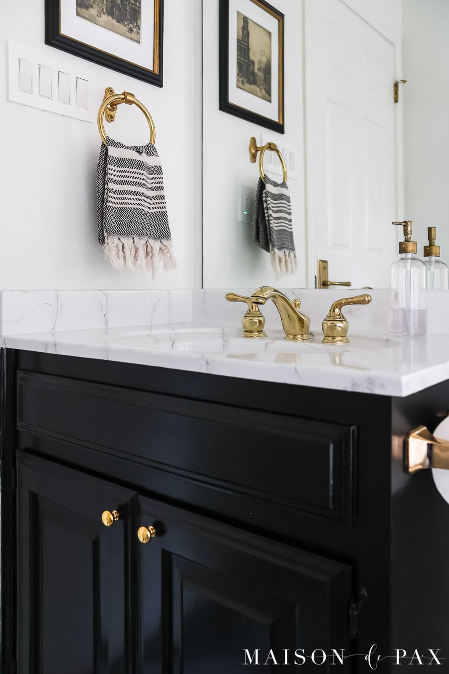 black glossy bathroom vanity with unlacquered brass knobs and faux marble countertop