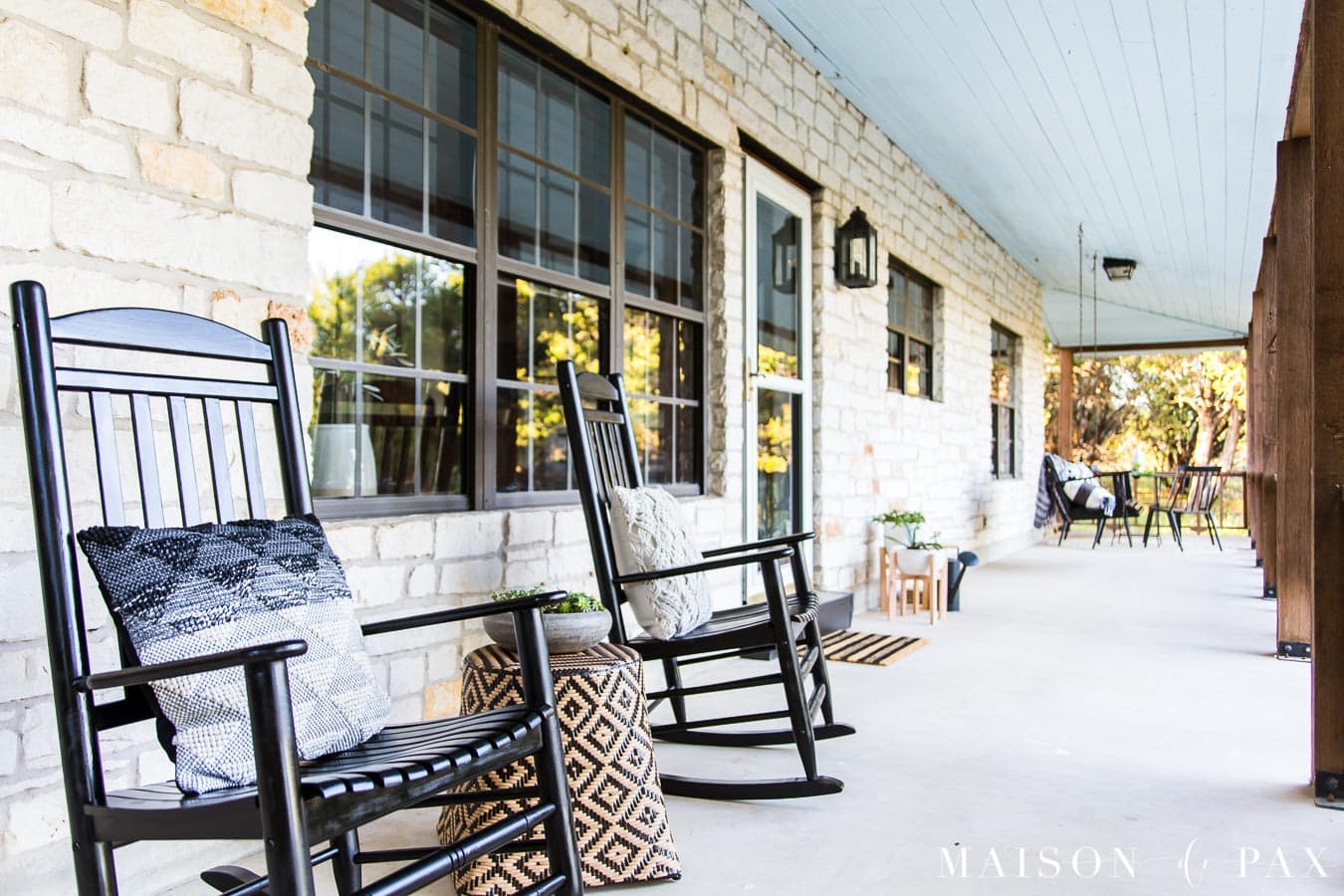 black rocking chairs on a porch with austin stone and black windows | Maison de Pax