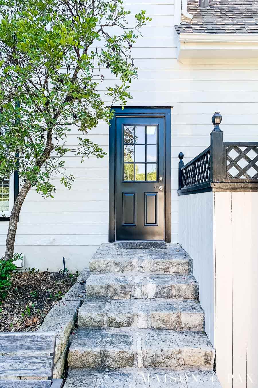 black door on house with white duck siding, white fence, and black lattice | Maison de Pax