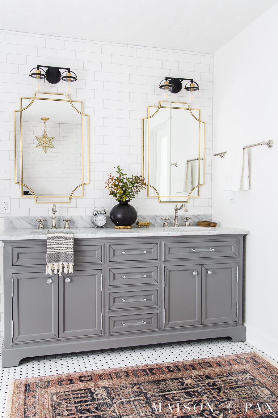 gray vanity in white tiled bathroom with polished nickel accessories and gold light fixtures