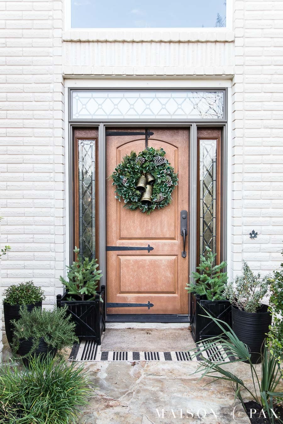 front porch with black planters and a festive holiday wreath with bells
