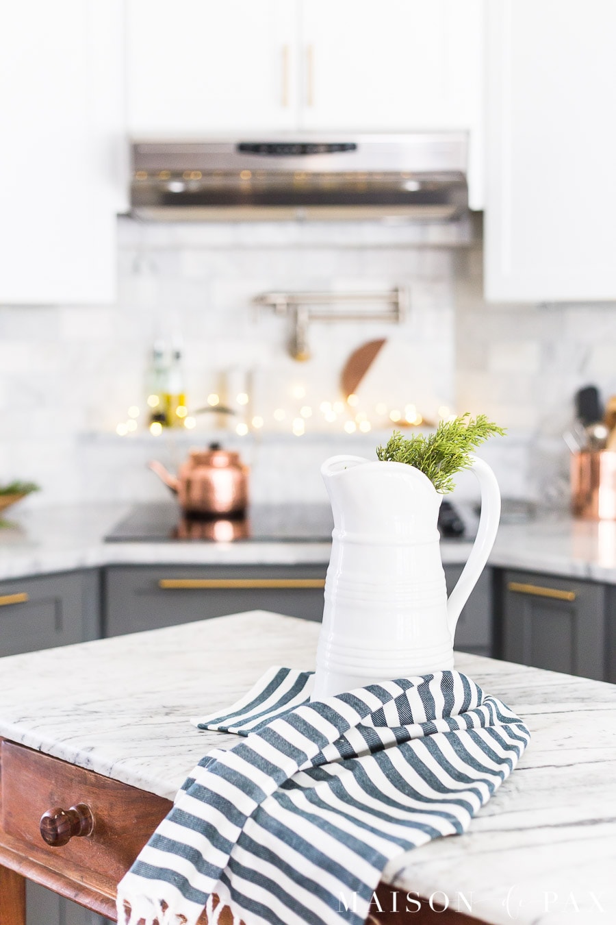 christmas kitchen: greenery in a farmhouse pitcher with a copper light strand in the background