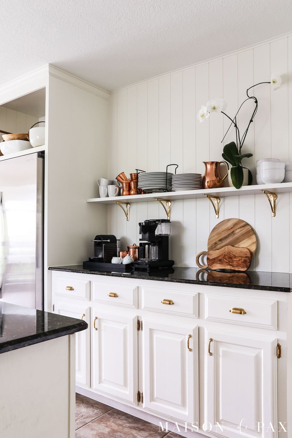 creamy white kitchen with vertical plank walls, open shelving, and black countertops