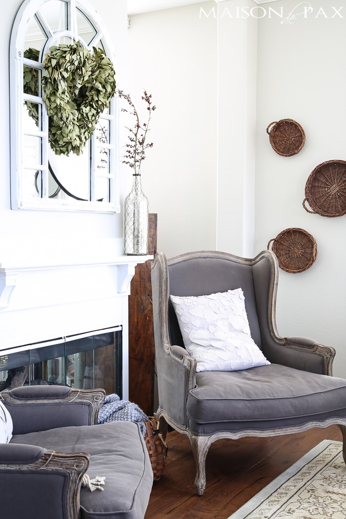 beautiful, neutral living room with gray wingback chairs, natural textures, white fireplace, and a gorgeous wreath 