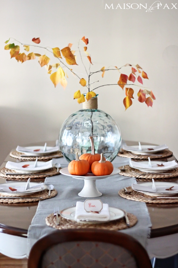 Lovely, simple Thanksgiving tablescape: a grand table and a side table with fall foliage centerpieces, simple neutral china settings, and a few pumpkins | aiweb9ygdry.cmersite.com