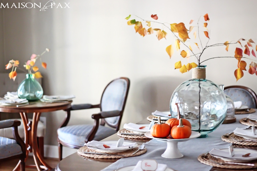 Lovely, simple Thanksgiving tablescape: a grand table and a side table with fall foliage centerpieces, simple neutral china settings, and a few pumpkins | aiweb9ygdry.cmersite.com