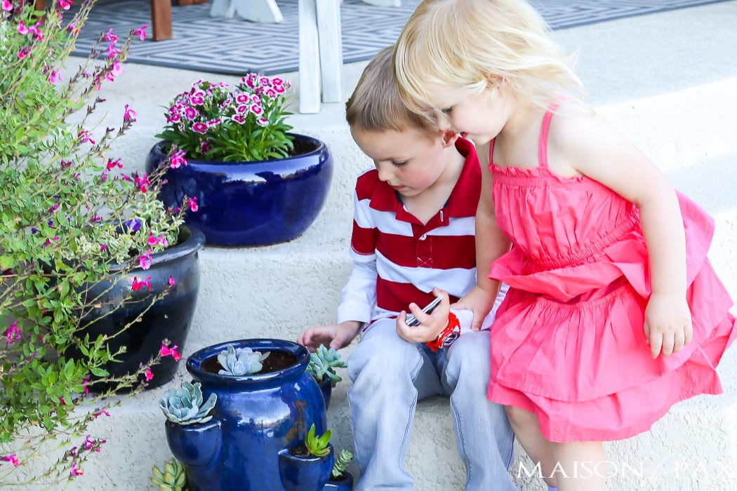 two small children sitting on a painted porch with spring planters- Maison de Pax