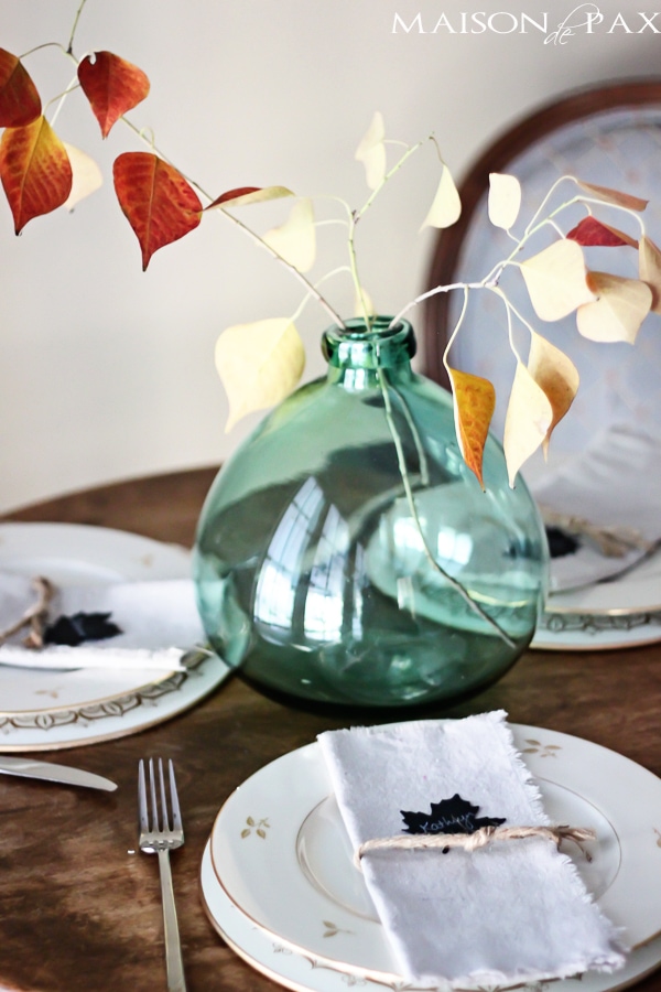 Lovely, simple Thanksgiving tablescape: a grand table and a side table with fall foliage centerpieces, simple neutral china settings, and a few pumpkins | aiweb9ygdry.cmersite.com