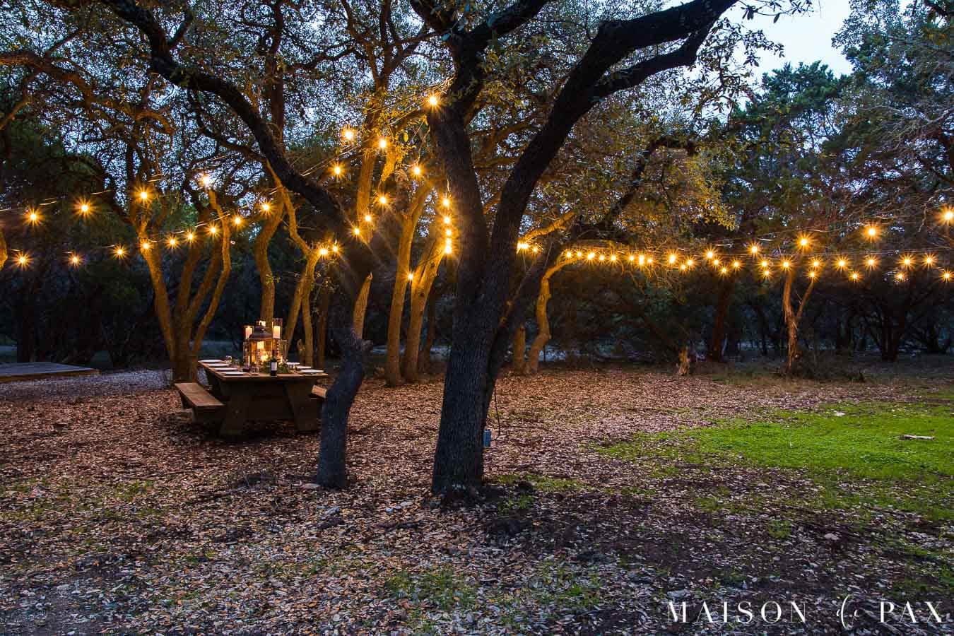 picnic table with globe lights strung through the trees | Maison de Pax