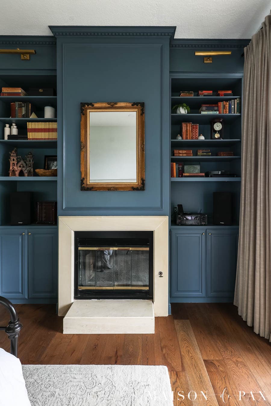 limestone fireplace flanked by bookcases with panel molding and dark blue paint